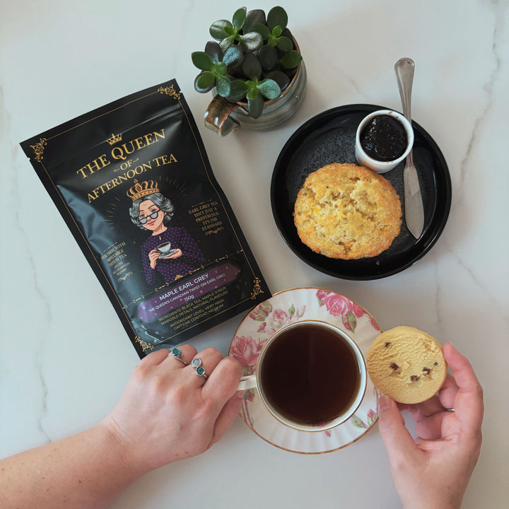 Translation missing: en.A top-down view of The Queen of Afternoon Tea holding a tea cup and a shortbread cookie, with a bag of Maple Earl Grey tea next to it, and a scone and jam on a plate on a white marble surface